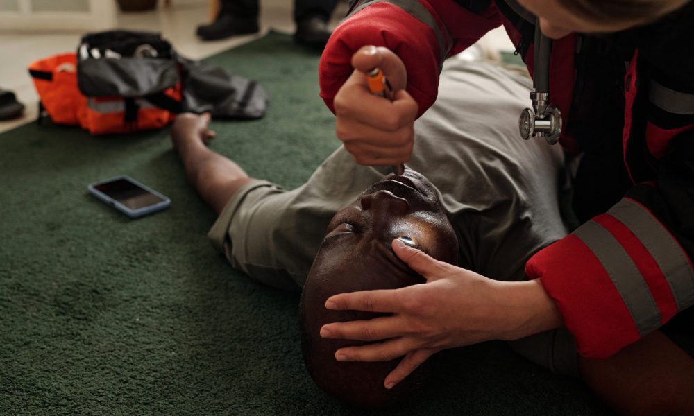 Emergency responder delivering critical first aid to unconscious individual lying on green carpet while utilizing medical device in home environment, emphasizing urgency of healthcare intervention